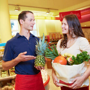 Verkäufer empfiehlt einer Kundin eine Ananas im Supermarkt