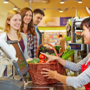 Junge Frau bezahlt Einkaufskorb mit Gemüse an der Kasse im Supermarkt